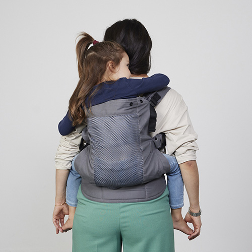 Woman carries toddler on her back in Izmi Breeze Toddler Carrier, back view